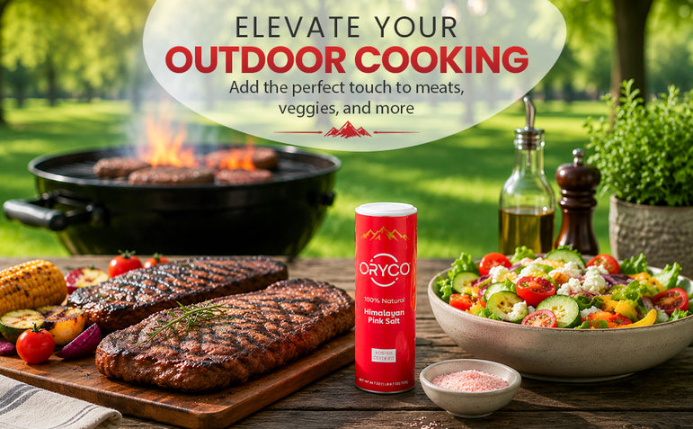 Outdoor cooking setup with grilled meats, salad, and a bottle of olive oil on a wooden table