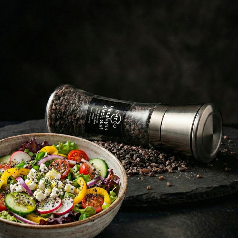 Pepper grinder next to a bowl of salad on a dark surface