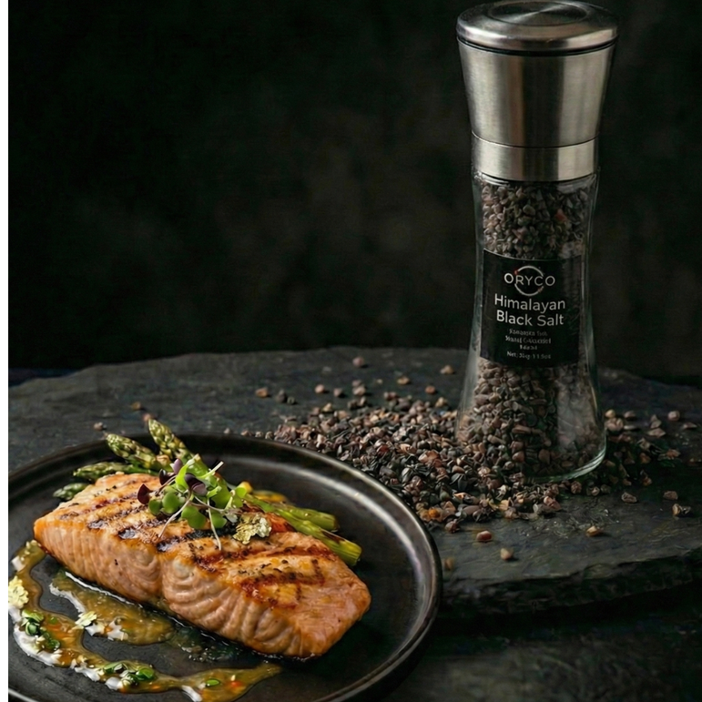 Grilled salmon with asparagus on a plate next to a pepper grinder on a dark surface