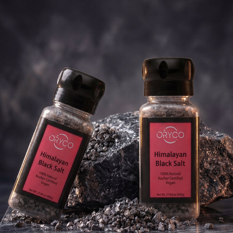 Two bottles of D'CO Himalayan Black Salt on a dark background with salt crystals around.